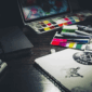 Edgy graphic design workspace with sketchbooks, color swatches, markers, and punk-style logo concepts under moody lighting
