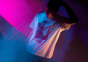 Person in a limited edition graphic tee under moody neon lighting, symbolizing exclusive merch and underground culture